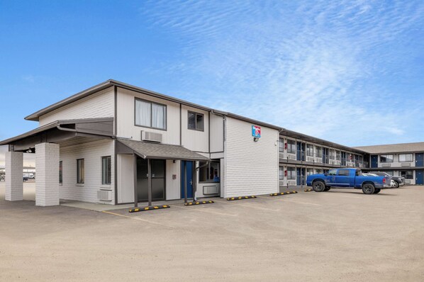 Ein Motel mit einstöckigem Gebäude, einem überdachten Parkplatz und einem blauen Lkw, der davor geparkt ist.