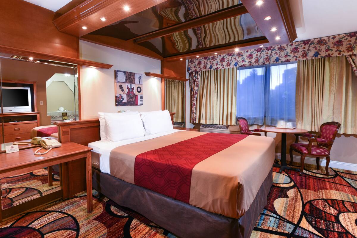 Ein Hotelzimmer mit einem großen Bett, einem Schreibtisch mit Telefon, einem Stuhl, einem kleinen Tisch und einem Fenster mit Vorhängen.
