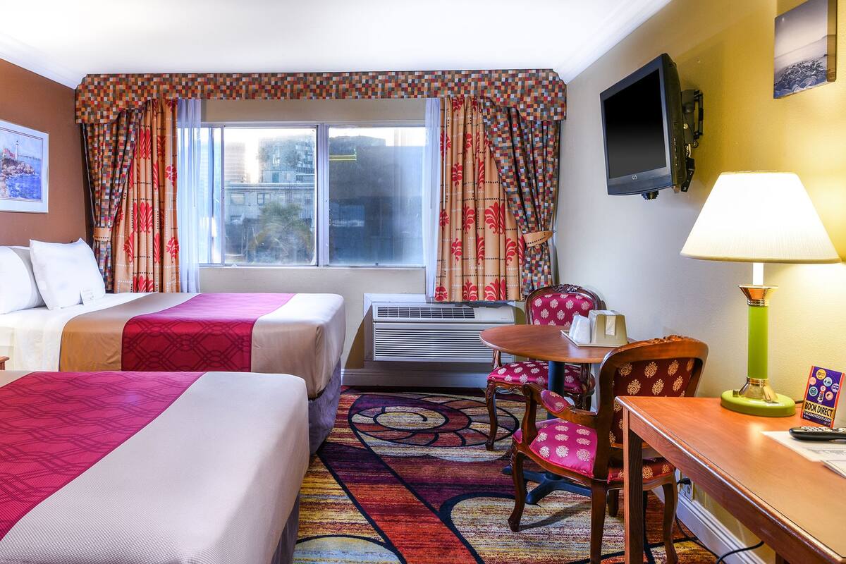 Ein Hotelzimmer mit zwei Betten, einem Schreibtisch, einem Sessel, einem Fernseher und einer Klimaanlage.
