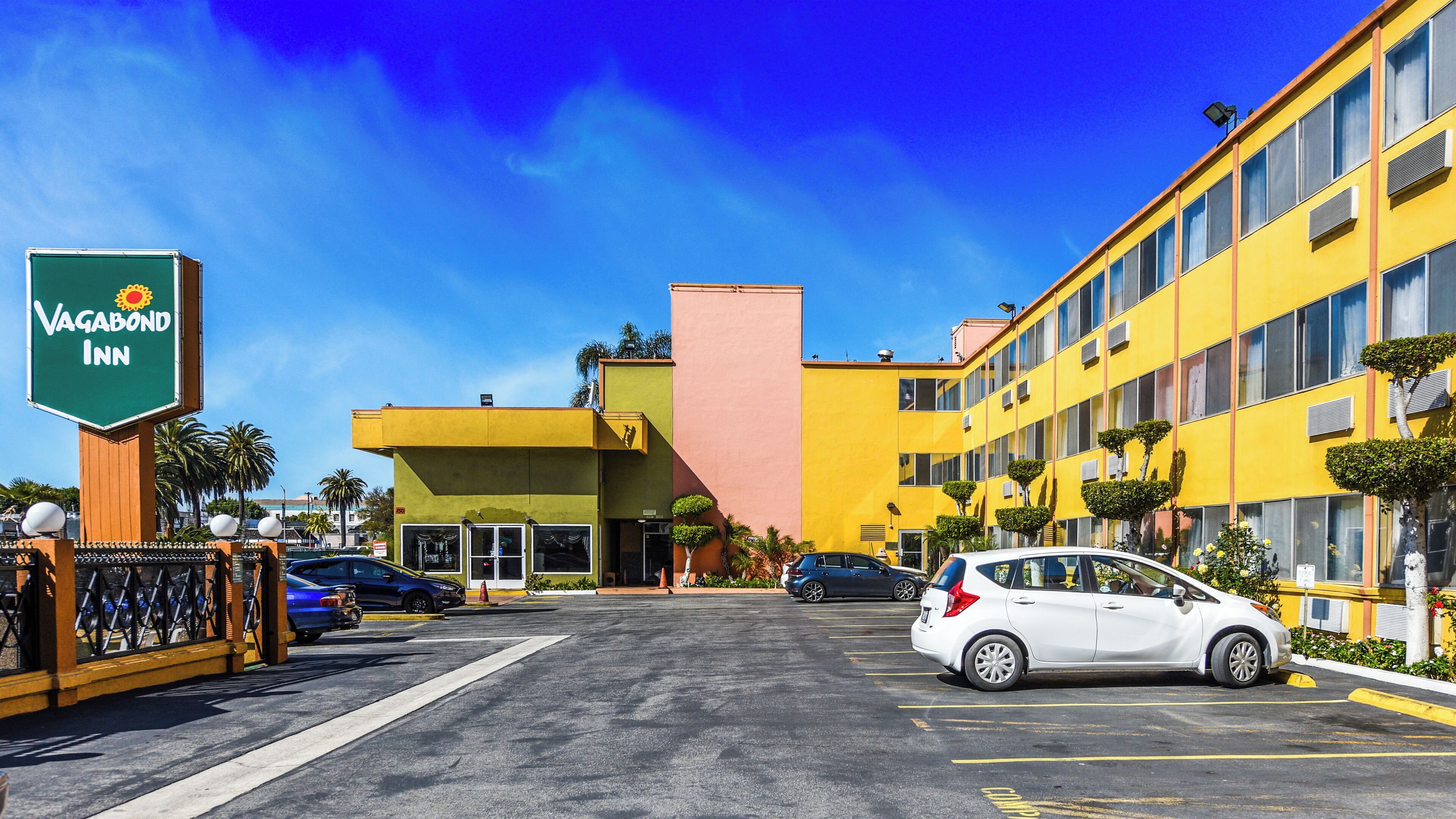 Un hôtel avec une enseigne verte, un parking et un bâtiment jaune.