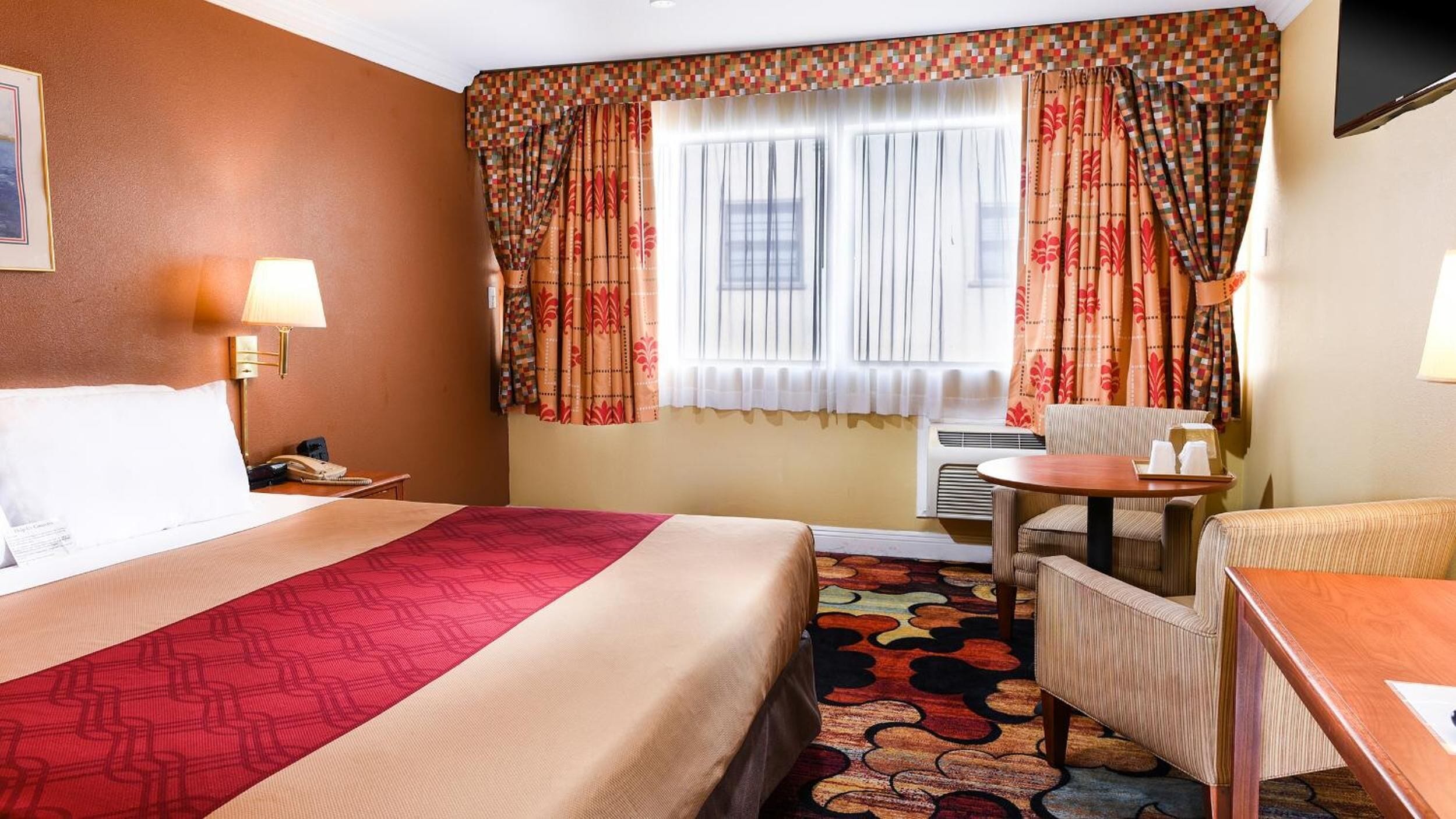 A hotel room with a large bed, a desk, a chair, and a window with curtains.