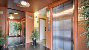 Een hotel lobby met een gepoetste vloer, houten wanden en twee liften. Er staan borden die de locatie van de ijsmachine en een rookvrij gebied aangeven.