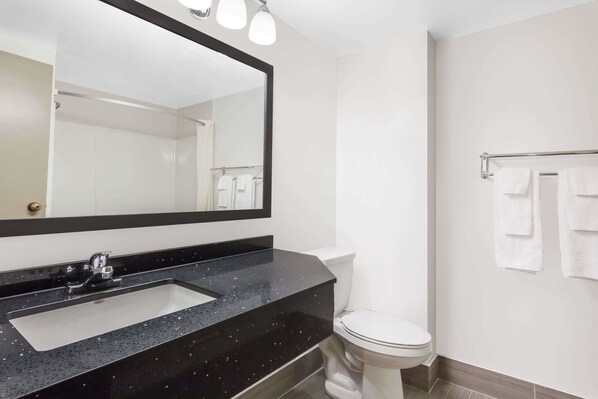 A bathroom with a black countertop sink, a white toilet, and a towel rack with white towels.