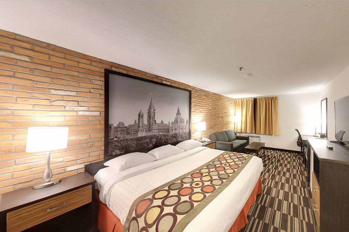 Ein Hotelzimmer mit Backsteinwand, einem Bett mit gemustertem Überwurf, einem Schreibtisch mit Fernseher und einem Sessel.