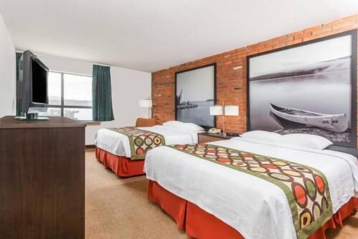 Une chambre d’hôtel avec deux lits, une télévision, une grande fenêtre et une fresque représentant un bateau.
