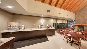 Un vestíbulo de hotel con mostrador de recepción, estación de café y zona de comedor con mesas y sillas de madera.