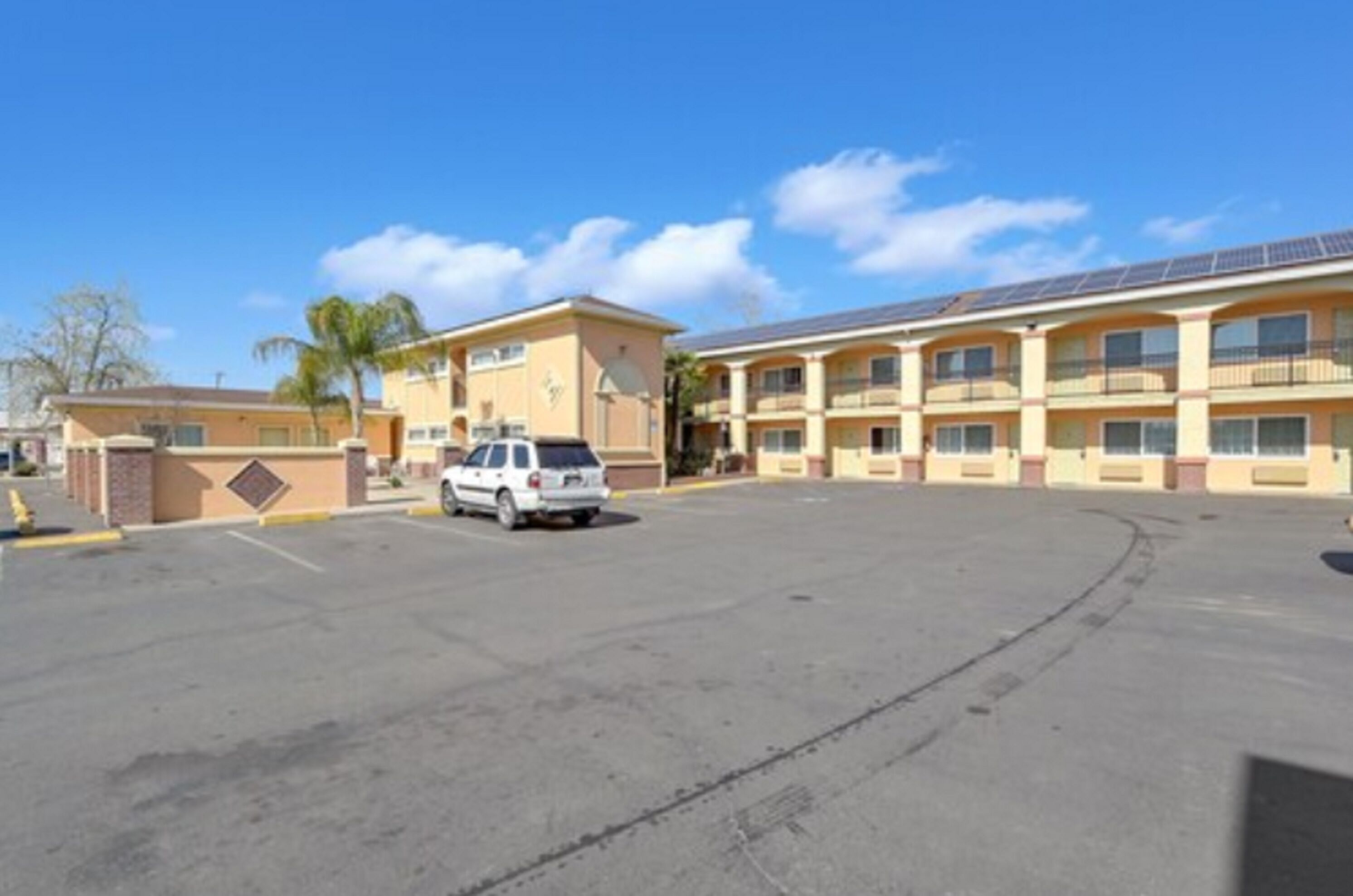 A hotel with a parking lot, a white SUV parked, and a building with multiple balconies.