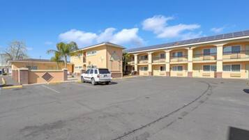 A hotel with a parking lot, a white SUV parked, and a building with multiple balconies.