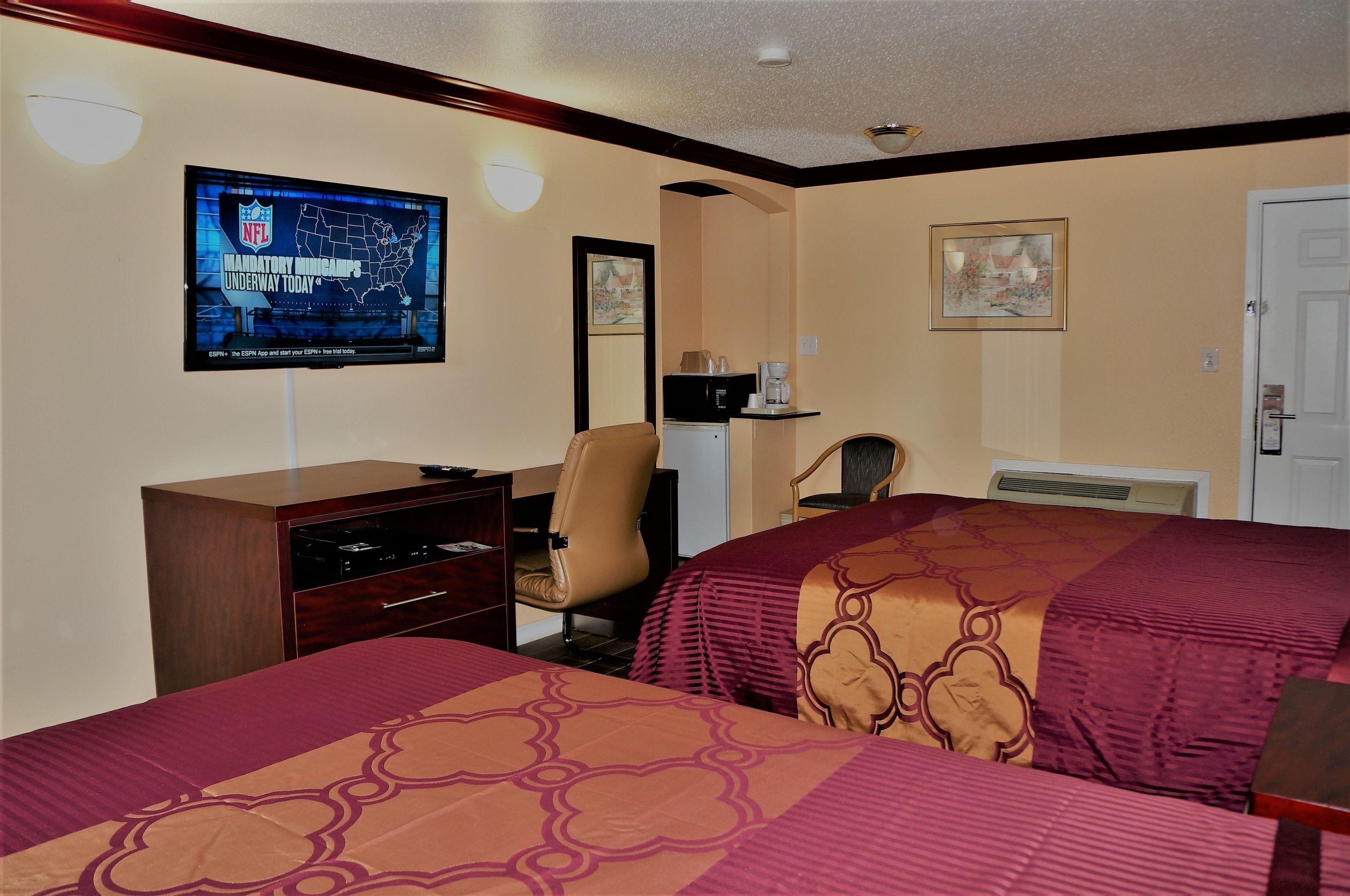 A hotel room with two beds, a television mounted on the wall, a desk with a chair, and a coffee maker.