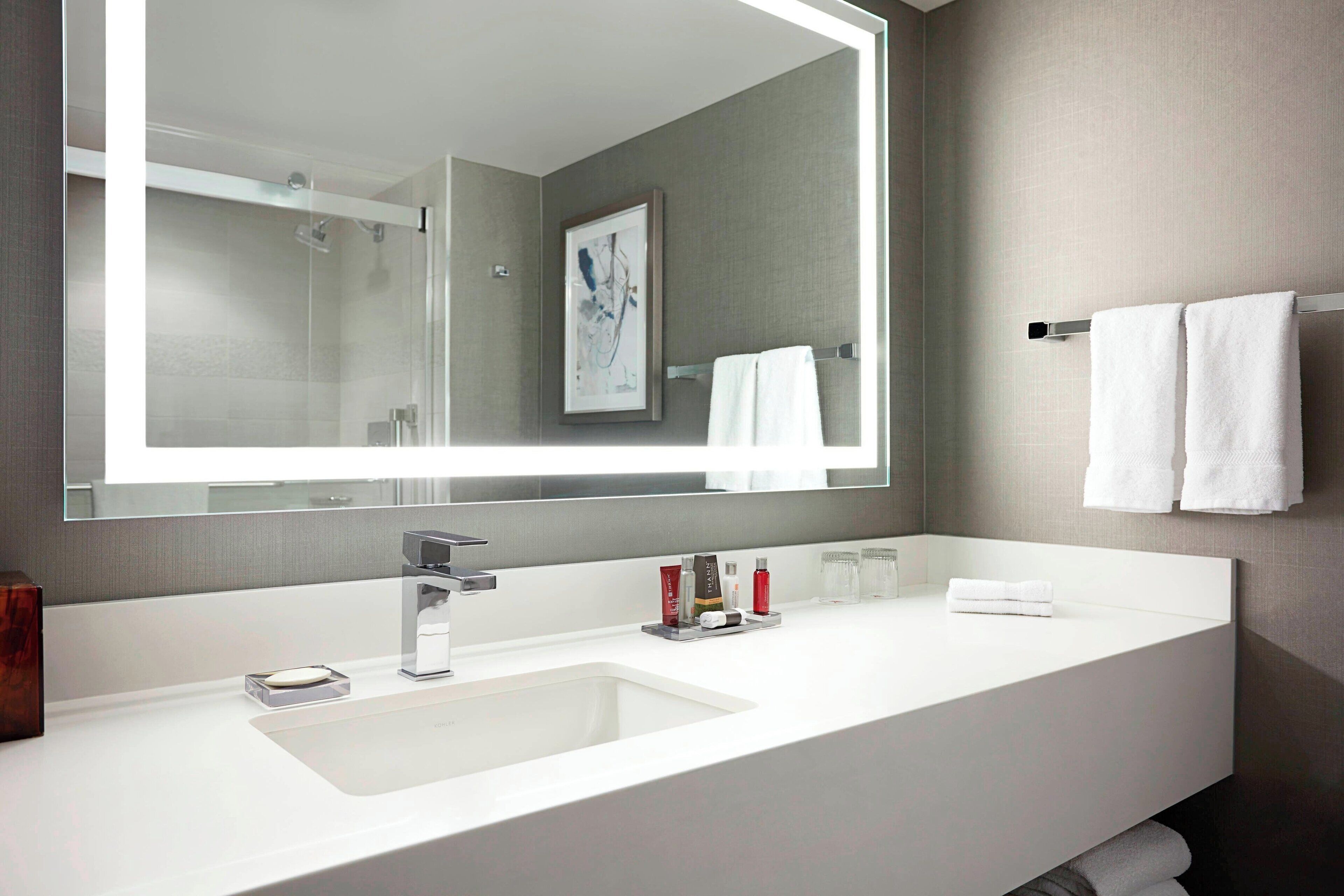 A modern bathroom with a large mirror, white sink, and towel rack.