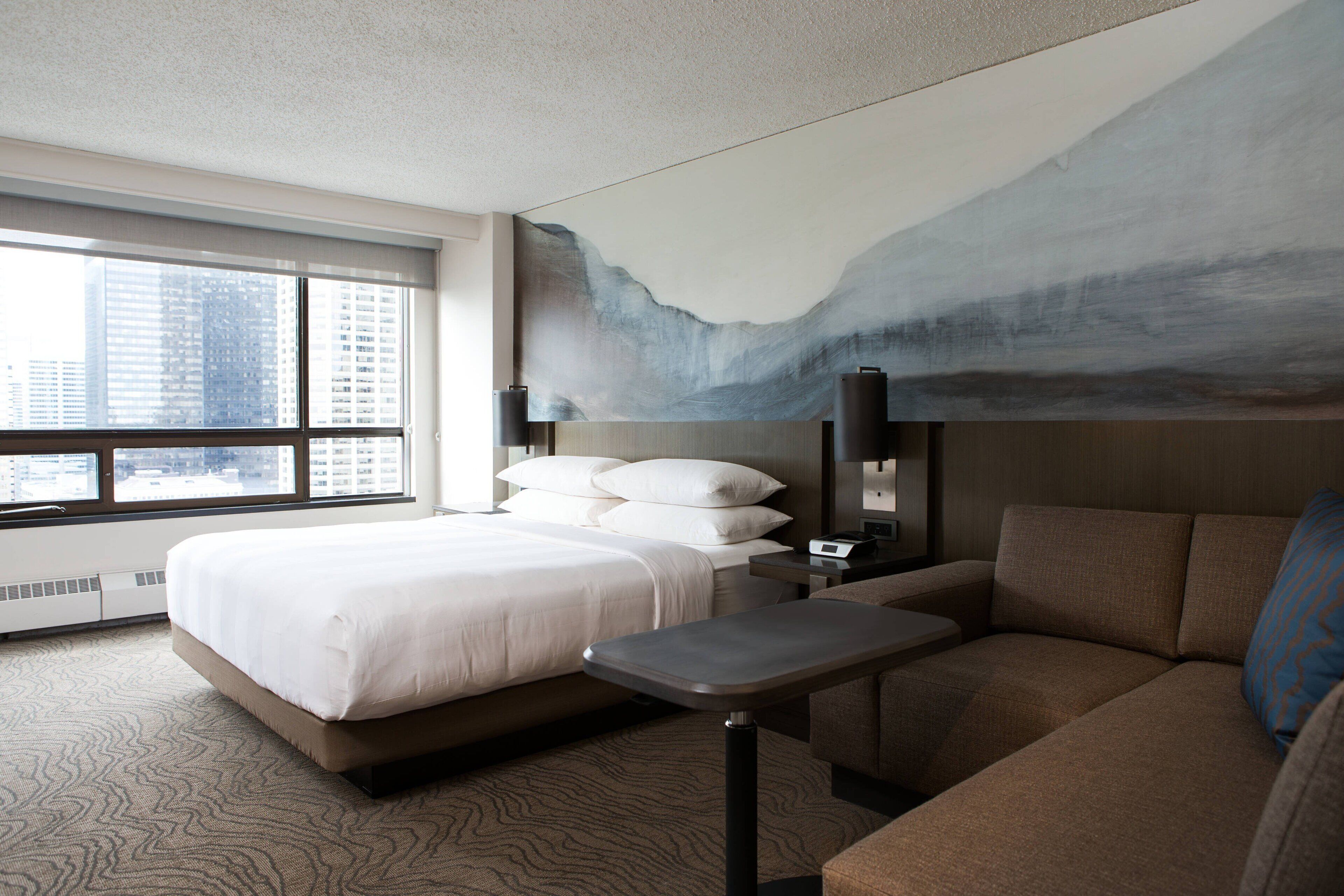 A hotel room with a large bed, a sofa, a small table, and a painting on the wall.