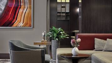 A modern living room with a grey armchair, a red sofa, a coffee table, and a large abstract painting on the wall.