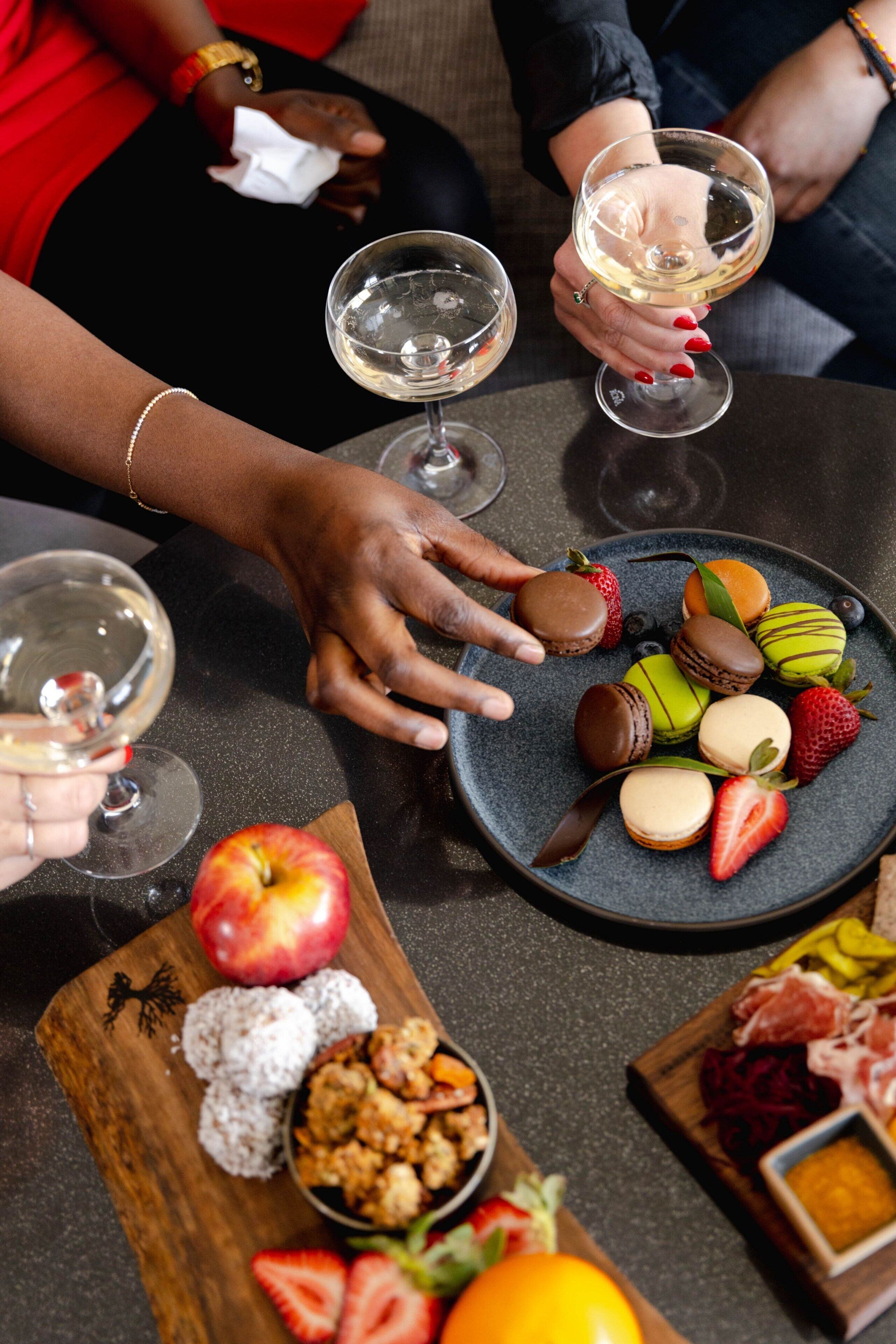 A table with a variety of food items and drinks, including a plate of macarons, strawberries, and a bowl of nuts.