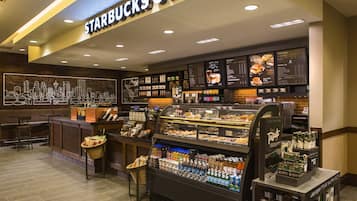 Interior de uma cafeteria Starbucks com um mural da paisagem urbana, diversas bebidas e uma vitrine de doces.