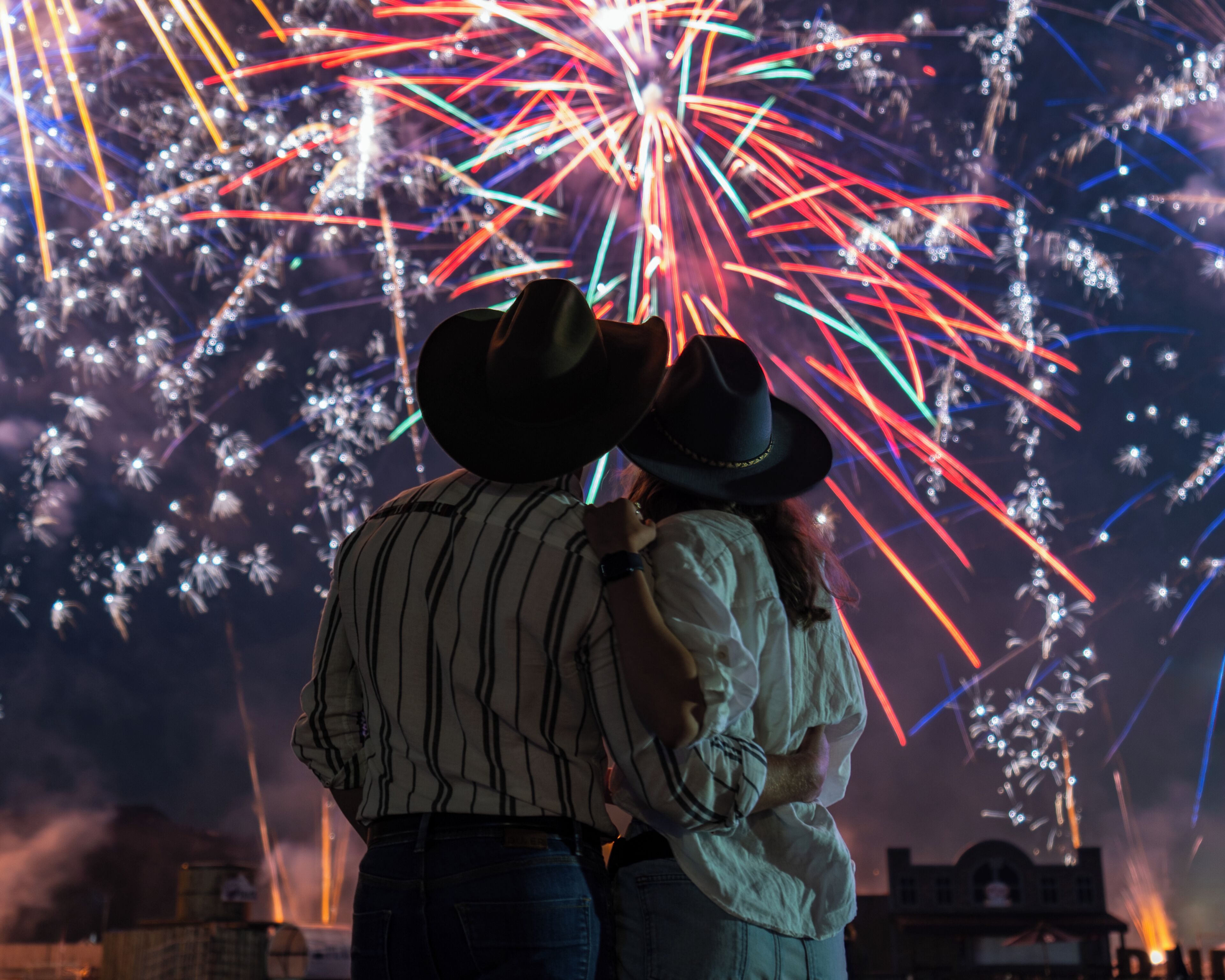 Un couple, portant des chapeaux de cow-boy, se tient devant un feu d’artifice.