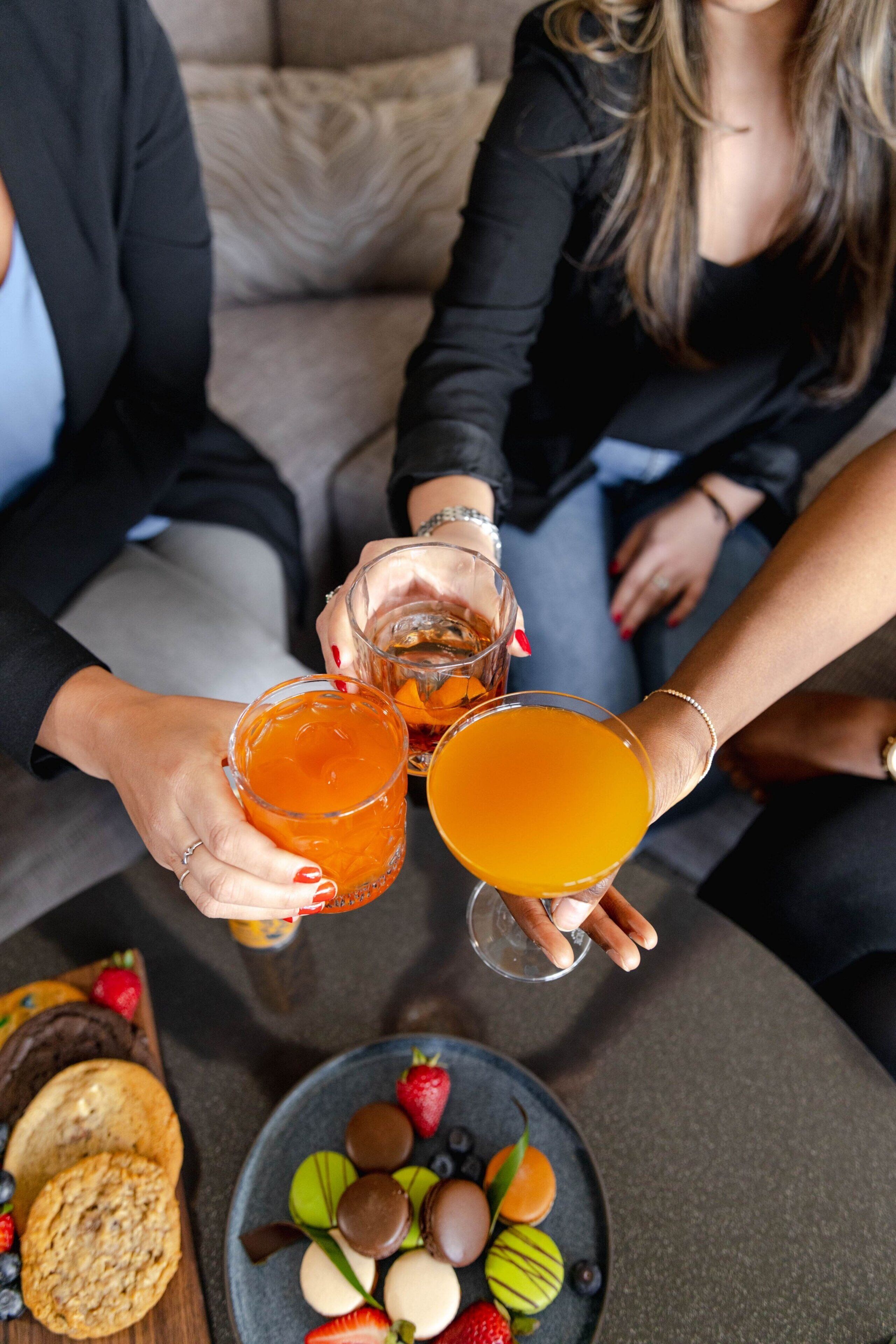 Un grupo de personas brindando con bebidas en una mesa con un plato de pasteles y galletas variados.
