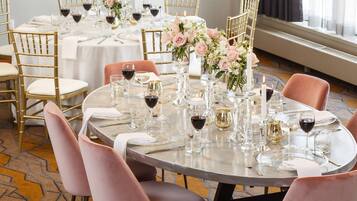 Une table de salle à manger ronde, préparée pour un repas formel, avec des chaises dorées, des nappes blanches et des chaises roses.