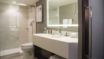 A modern bathroom with a shower, toilet, and a large mirror above the sink.