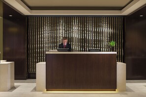 A reception desk with a dark wood finish, a man in a suit behind it, and a vertical striped wall behind.