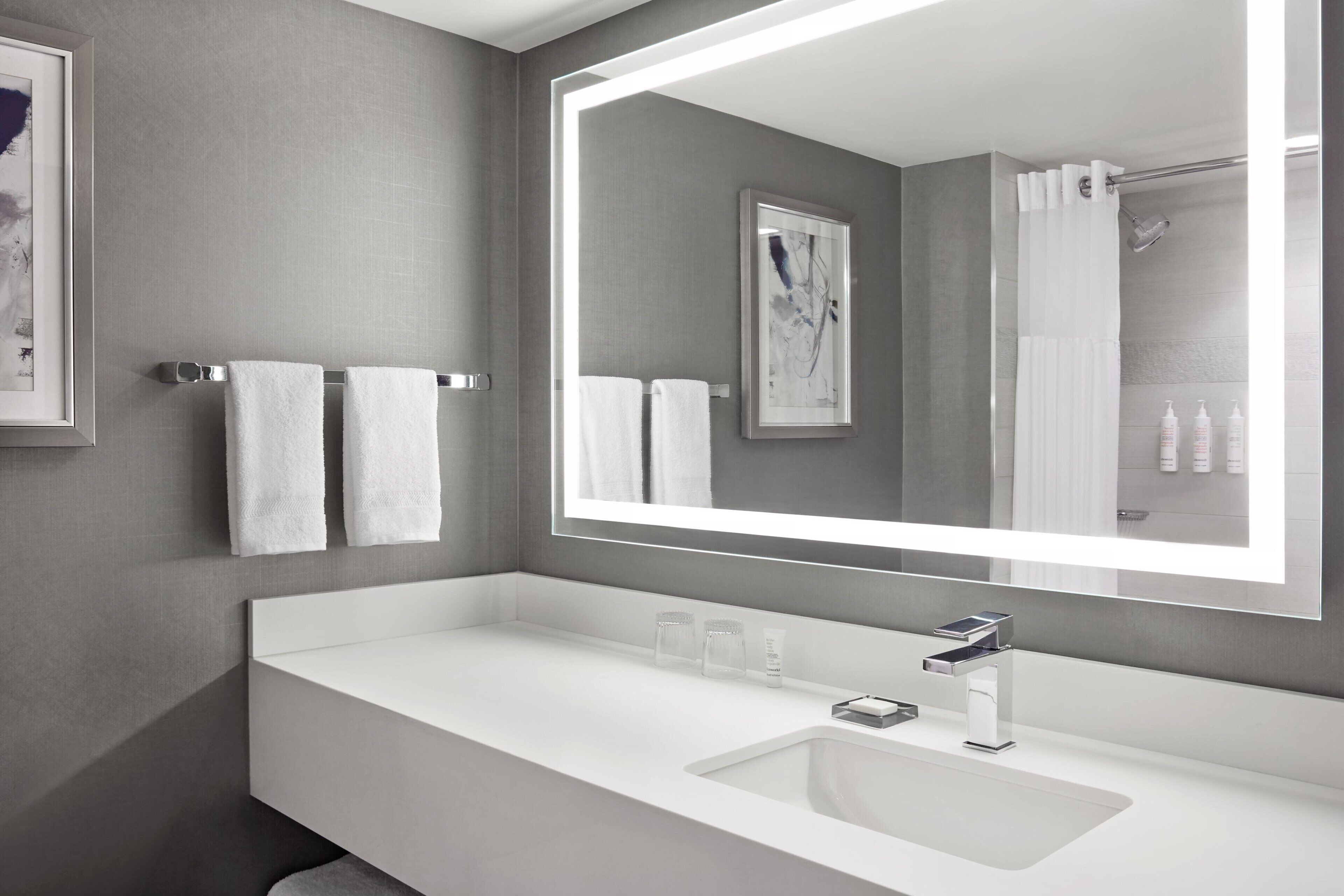 A modern bathroom with a large mirror, white sink, and two towels hanging on the wall.