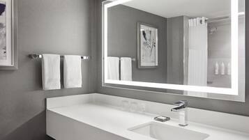 A modern bathroom with a large mirror, white sink, and two towels hanging on the wall.