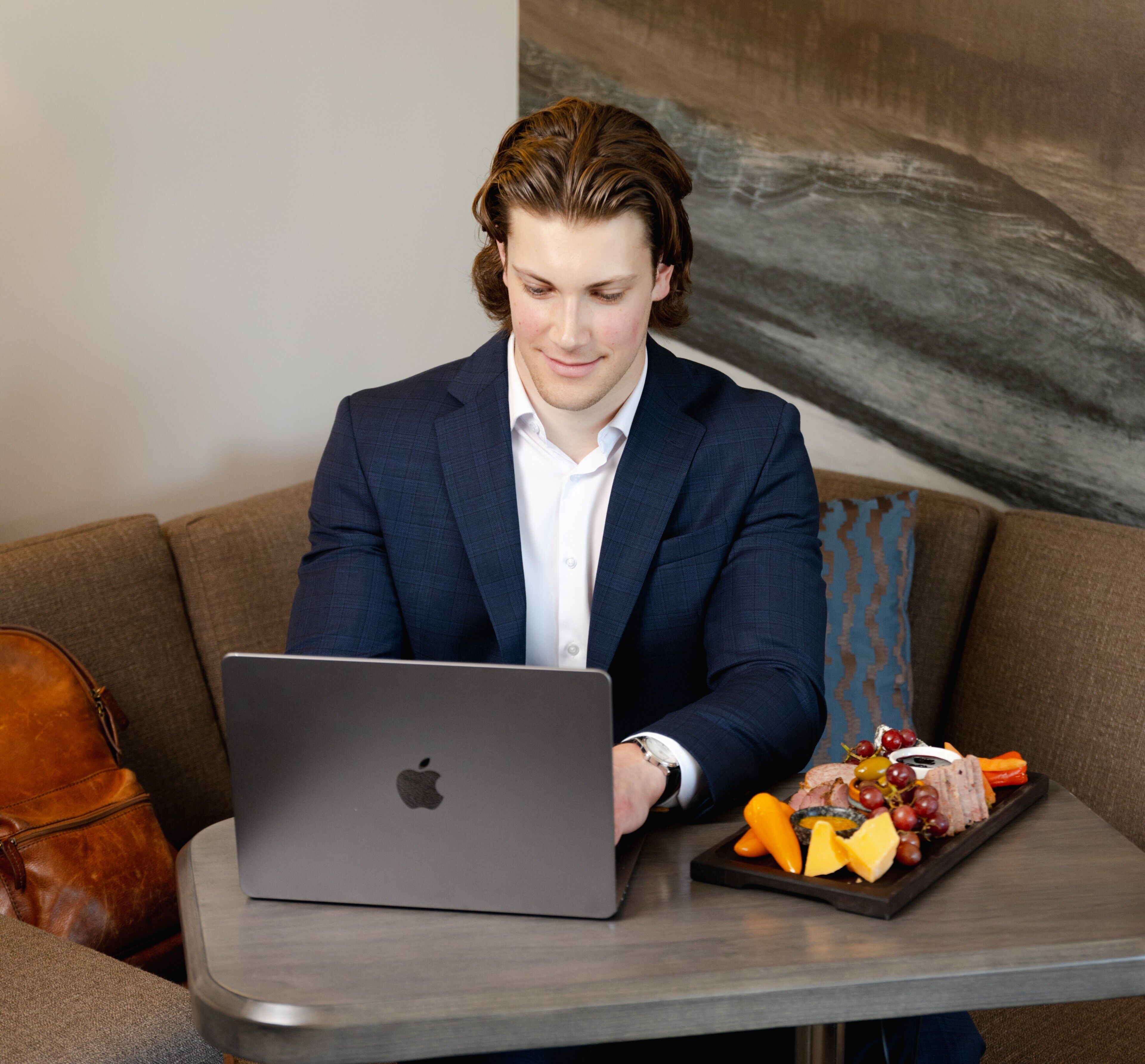 A person seated on a couch with a laptop and a tray of food.