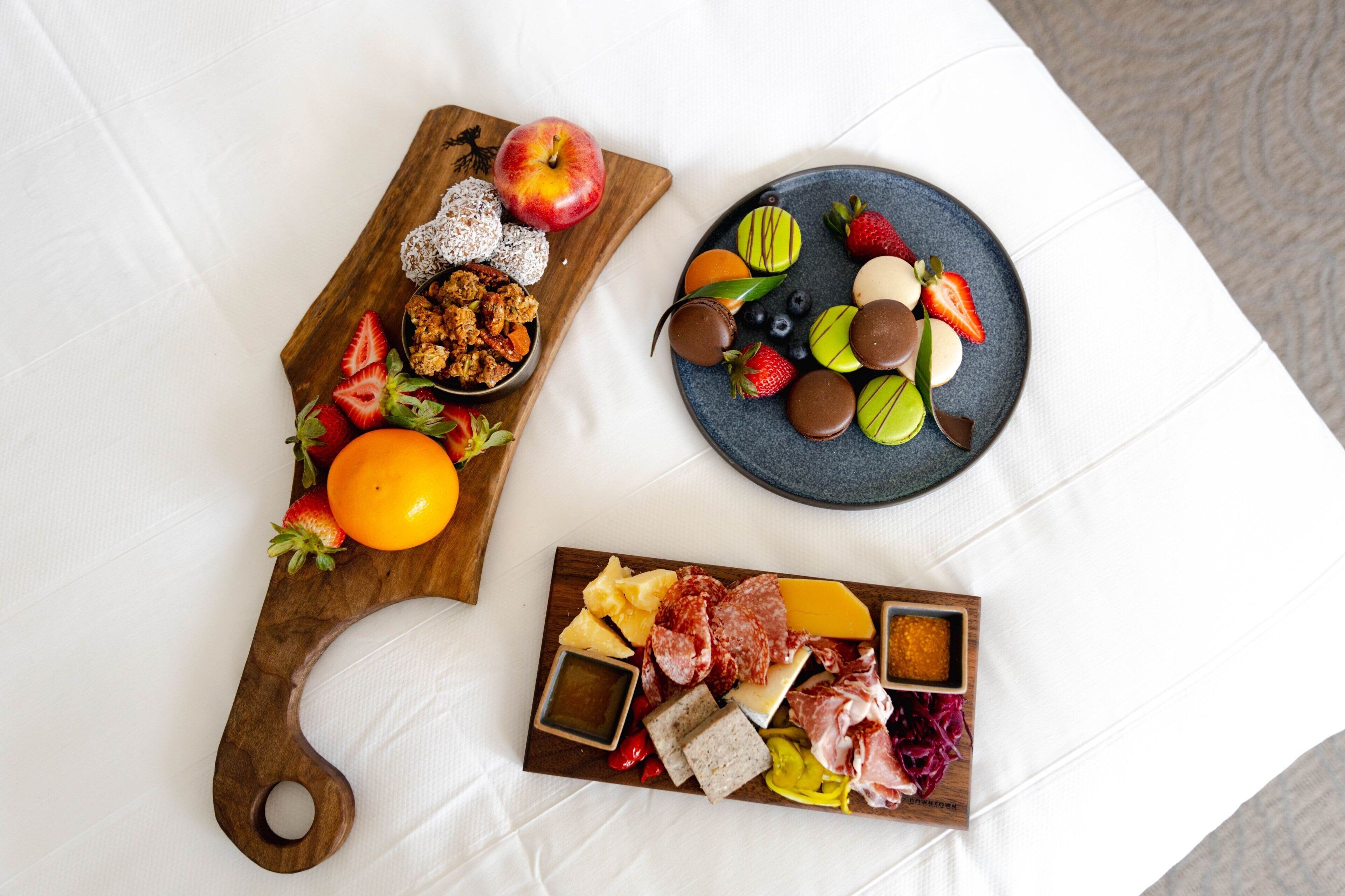 A wooden board with fruits, nuts, and cheese; a plate with chocolate and strawberries; and a smaller board with meats and cheeses.