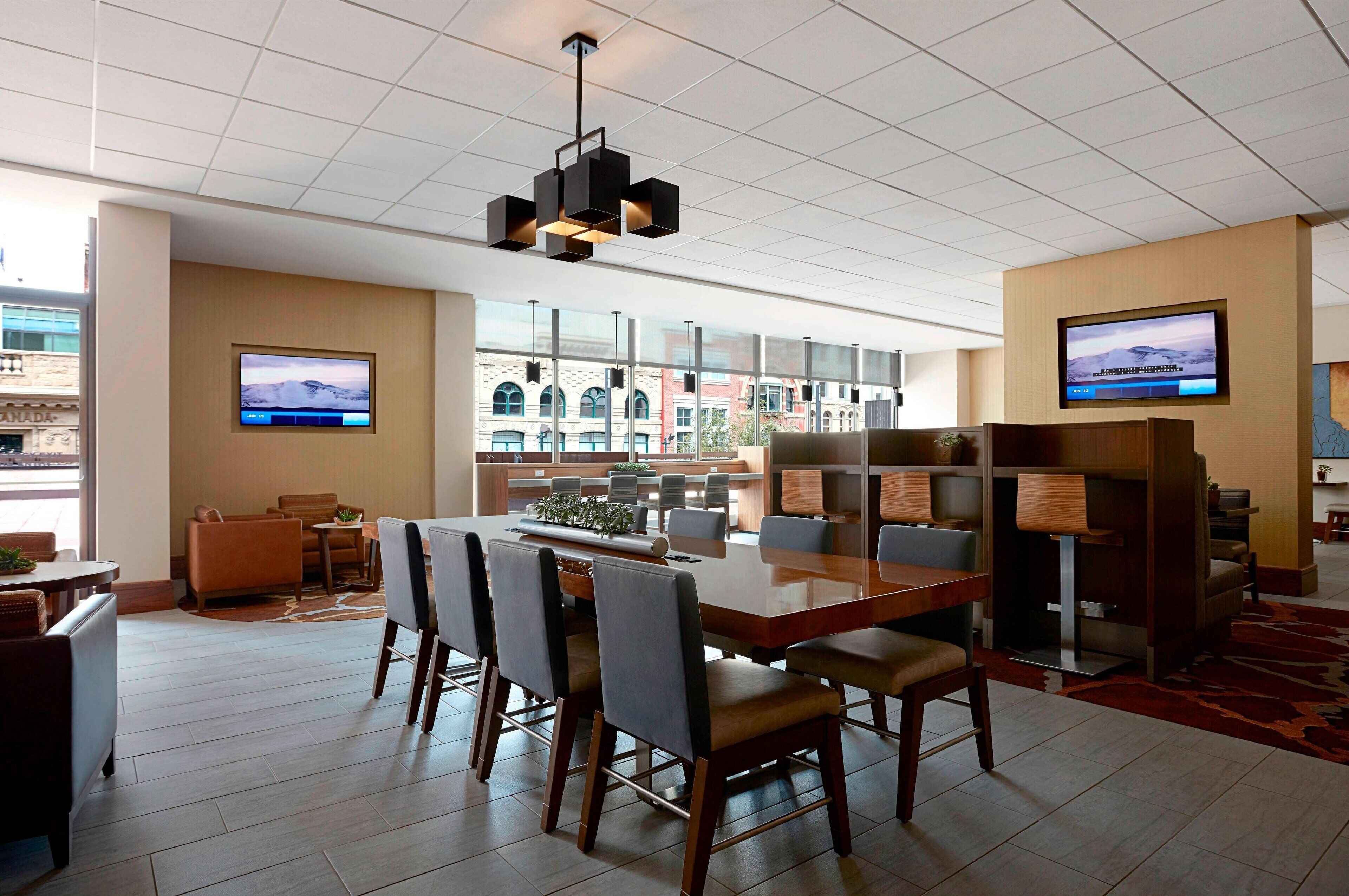 Un moderno vestíbulo de hotel con una amplia mesa de conferencias de madera, asientos cómodos y grandes ventanales con vistas a la ciudad.