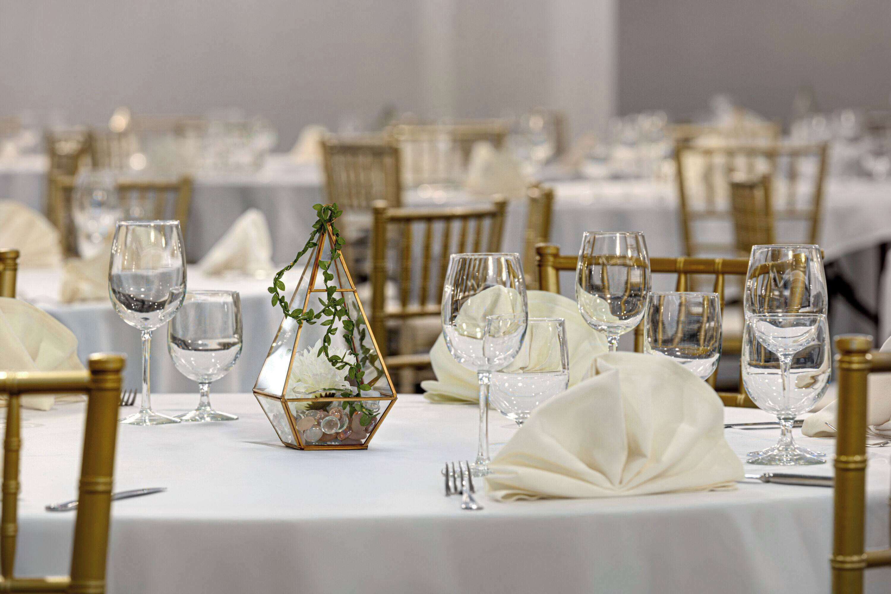 A banquet table set with white tablecloths, gold chairs, and clear glassware.