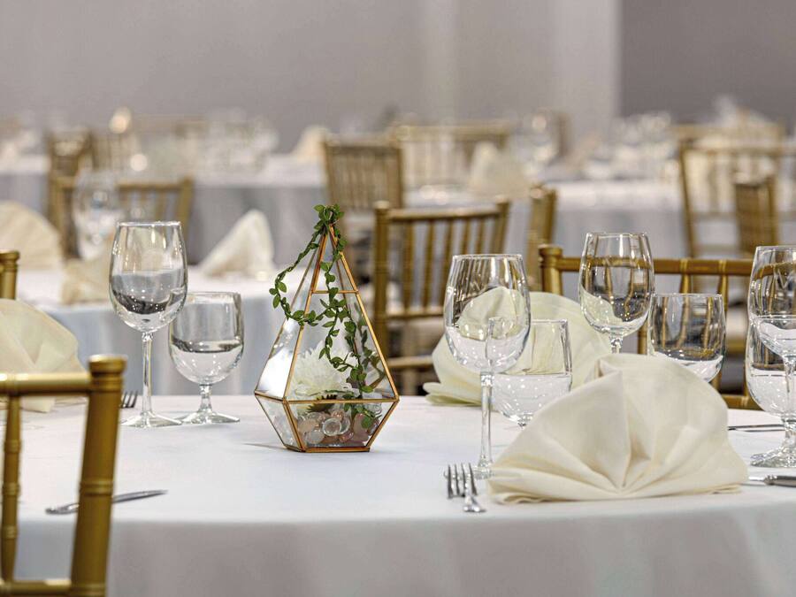A banquet table set with white tablecloths, gold chairs, and clear glassware.