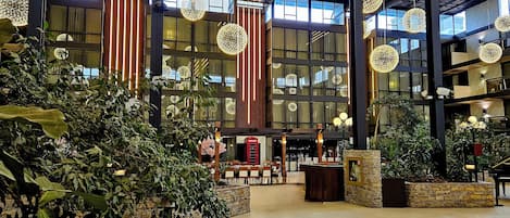 Um hall amplo com grandes janelas, luminárias esféricas penduradas e plantas internas.