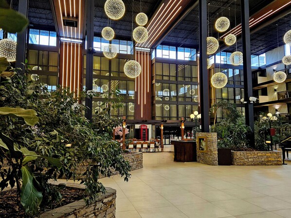 A spacious lobby with large windows, hanging spherical light fixtures, and indoor plants.