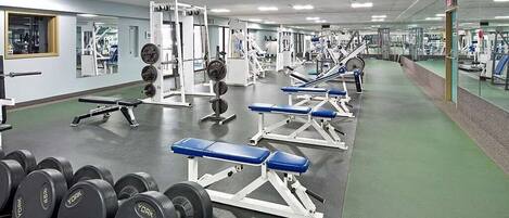 Un gimnasio con equipamiento de levantamiento de pesas, bancos y espejos.