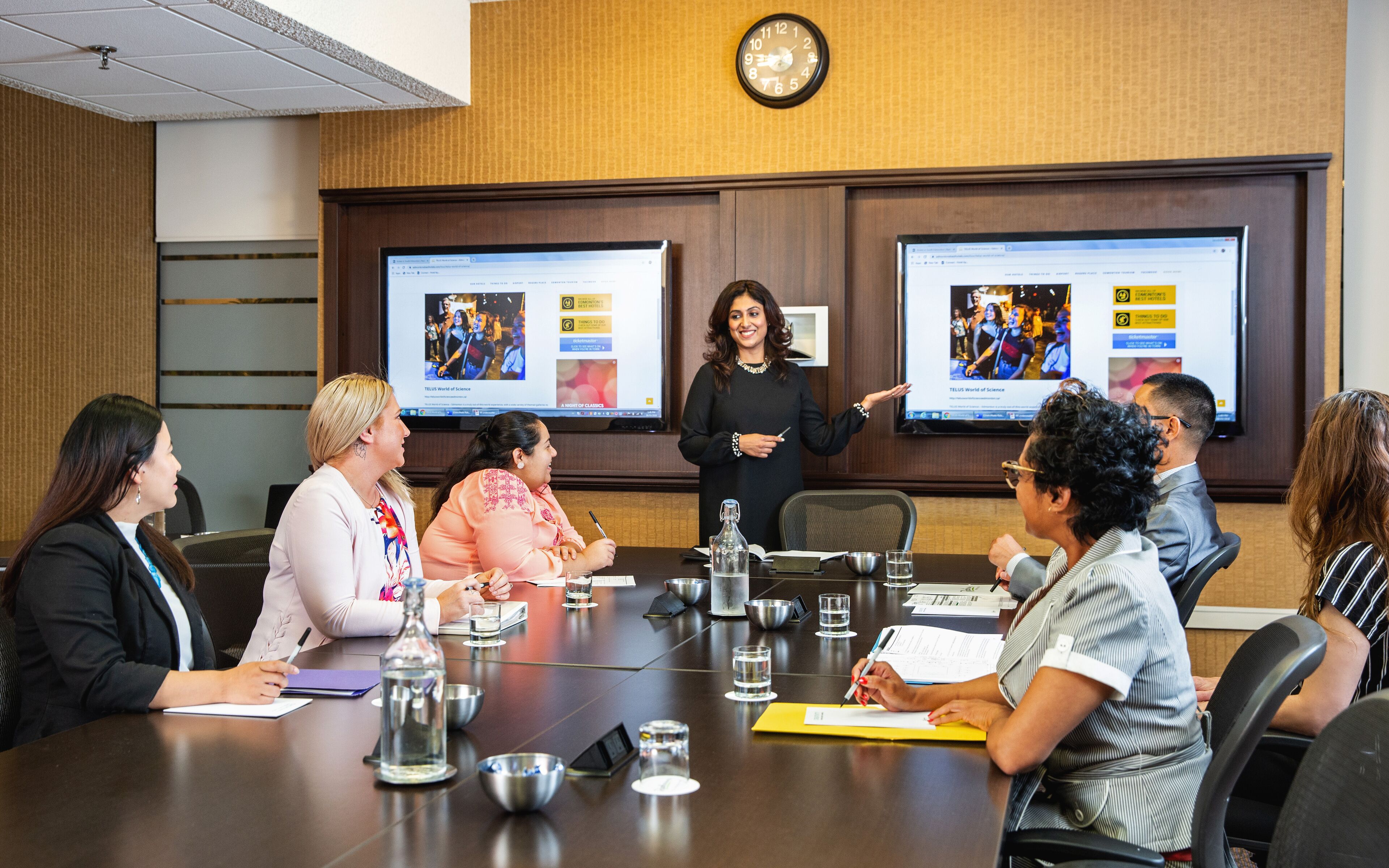 A conference room with a long table, multiple screens, and attendees engaged in a meeting.