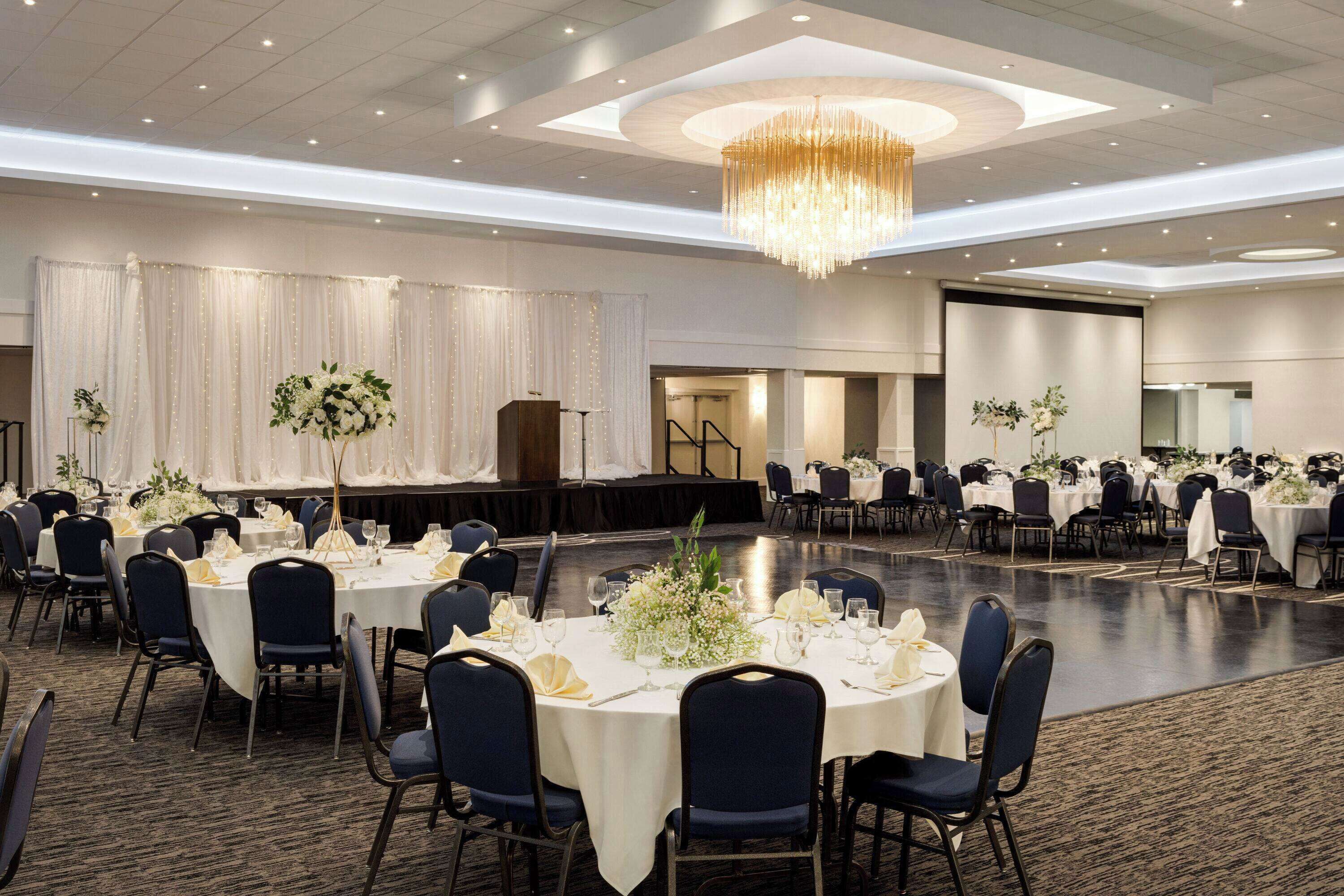 A banquet hall with round tables, chairs, and a stage.