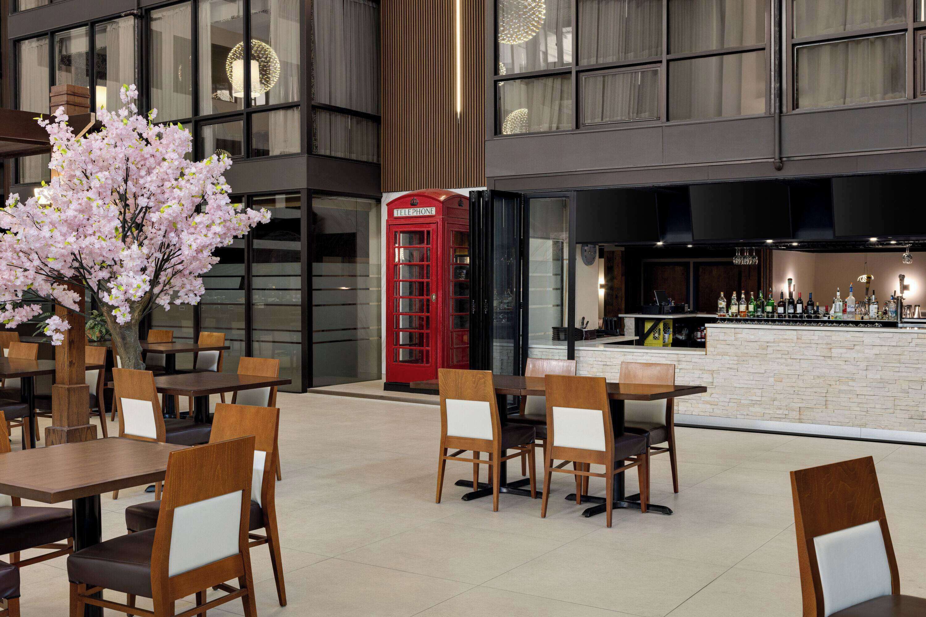 An indoor dining area with wooden tables and chairs, a red telephone booth, and a bar with a stone countertop.