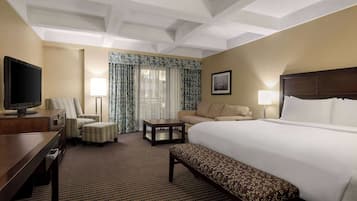 Une chambre d’hôtel avec un grand lit, un bureau avec une télévision, un canapé, un banc et une petite table.