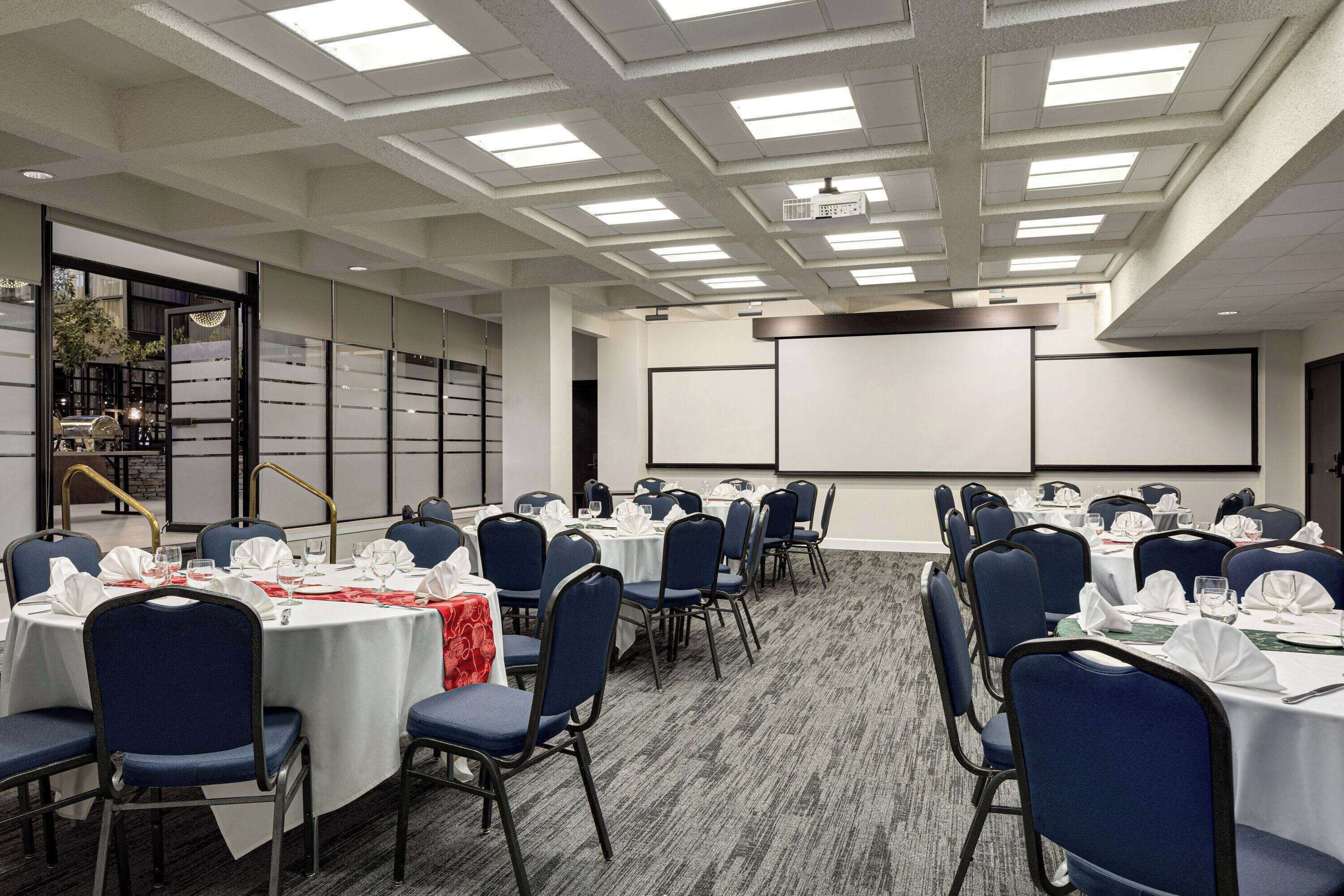 A conference room with round tables, blue chairs, and a projector screen.