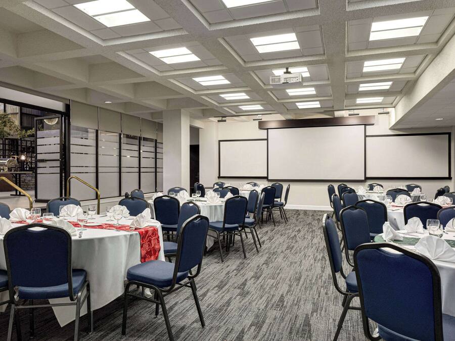 A conference room with round tables, blue chairs, and a projector screen.