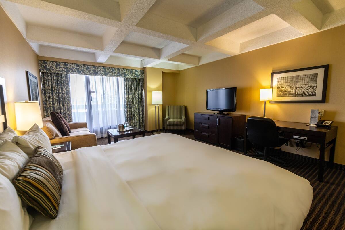 A hotel room with a large bed, a desk with a computer, a television, and a chair.