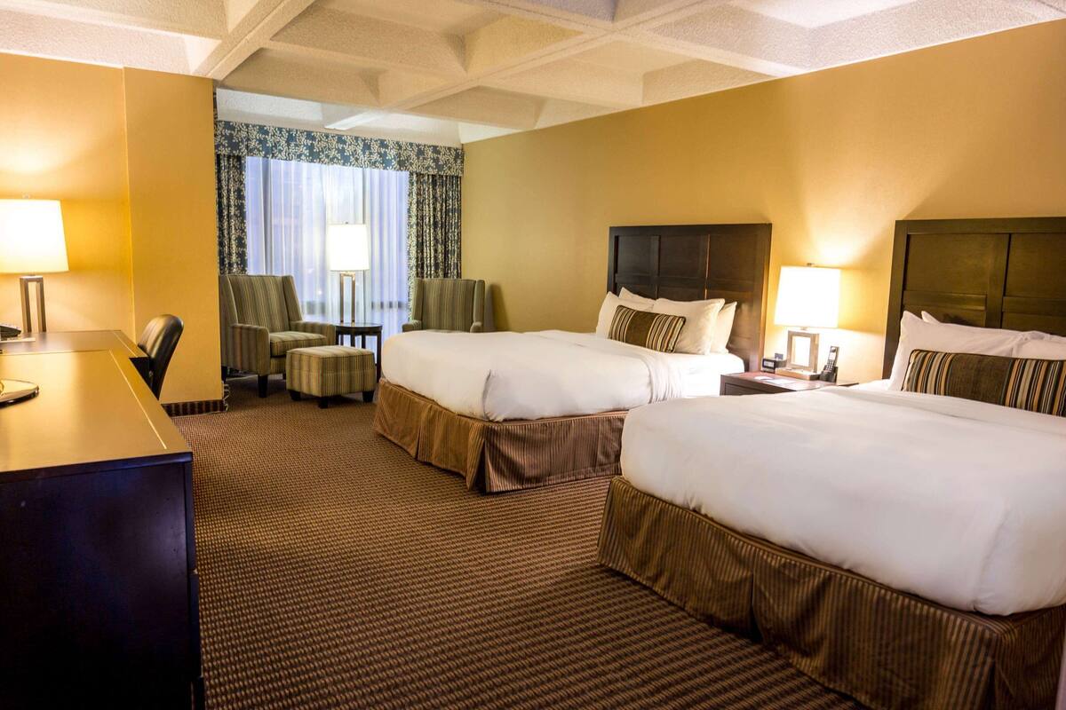 A hotel room with two beds, a desk, a chair, and a small table.