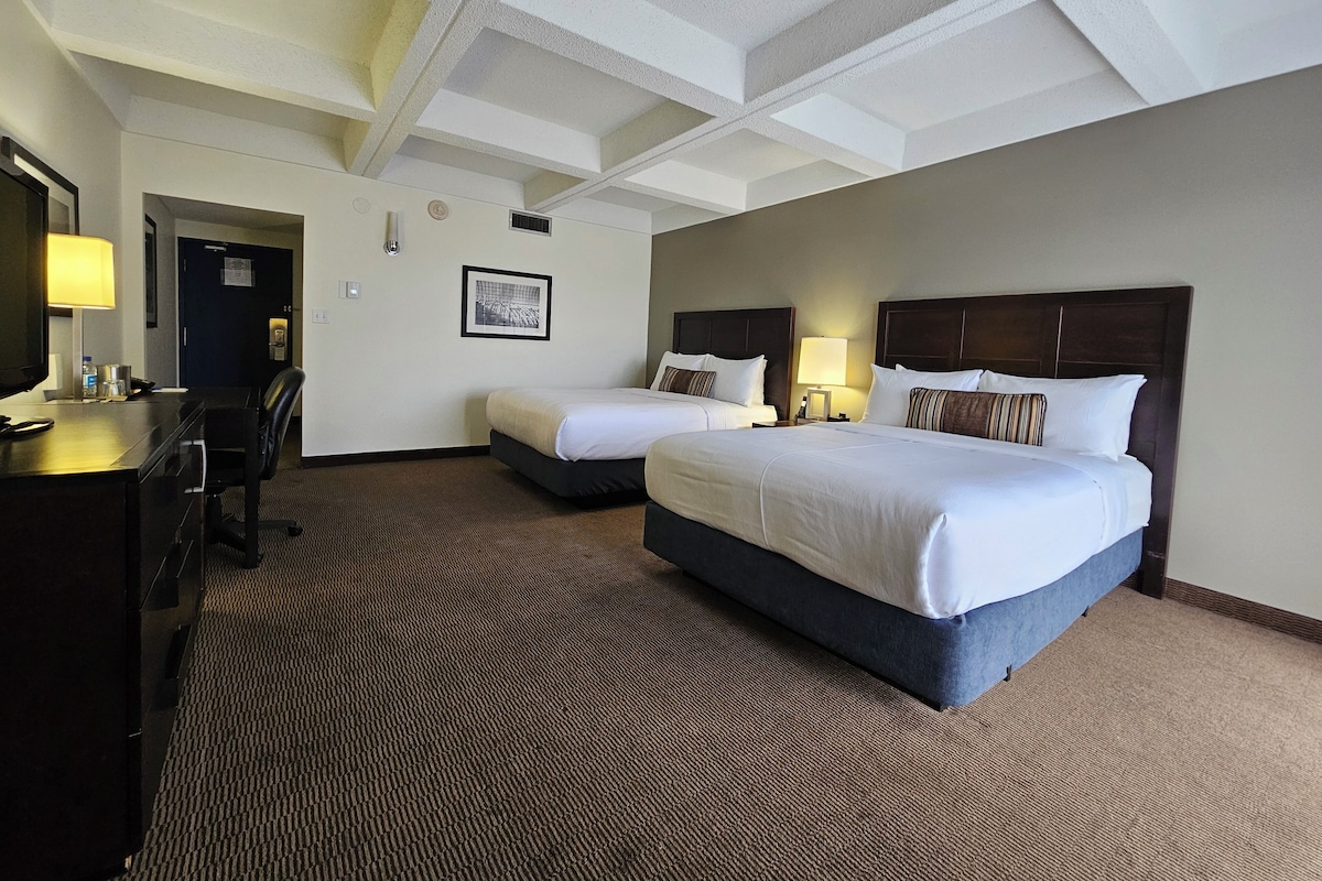 A hotel room with two beds, a desk, and a television.