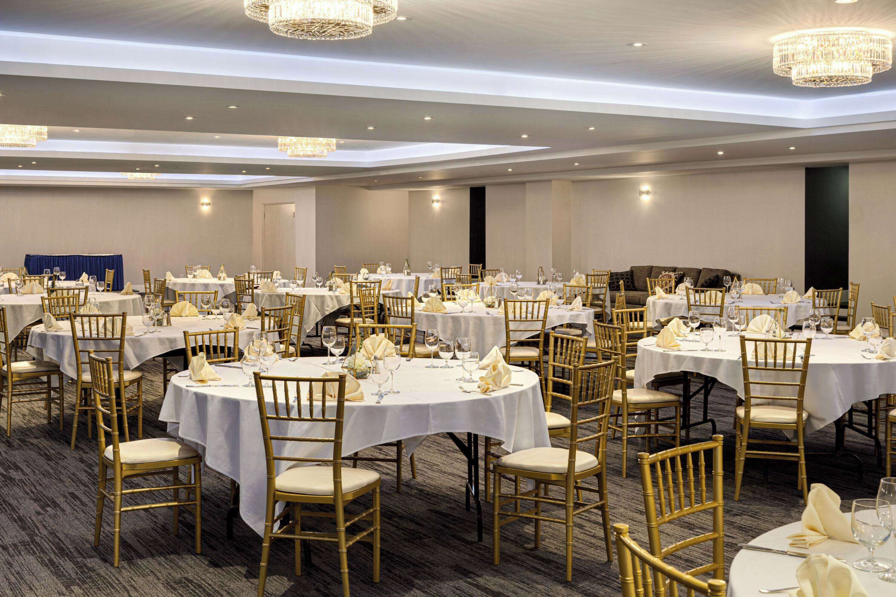 A banquet hall with round tables, gold chairs, and white tablecloths.
