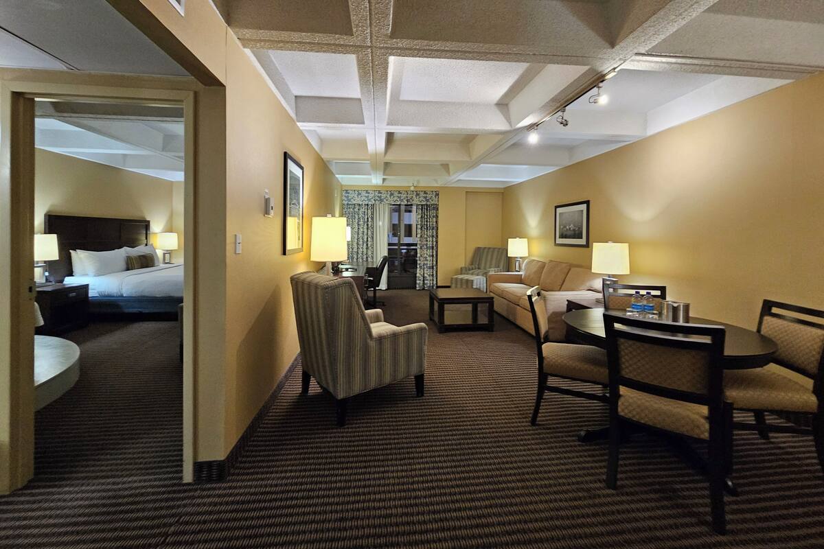 A hotel room with a bed, a desk, a chair, a sofa, and a dining table.