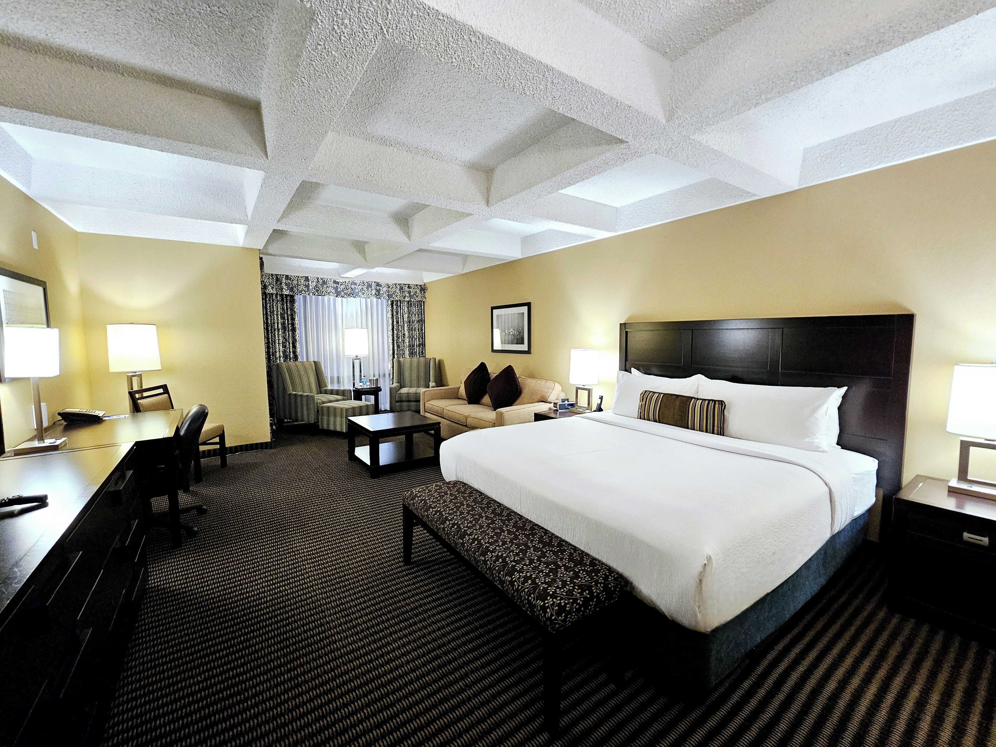 Habitación de hotel con una cama grande, un escritorio con silla, un sofá y una mesita.