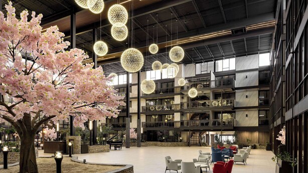 Un vestíbulo amplio con un gran árbol, zonas de estar y luminarias modernas.