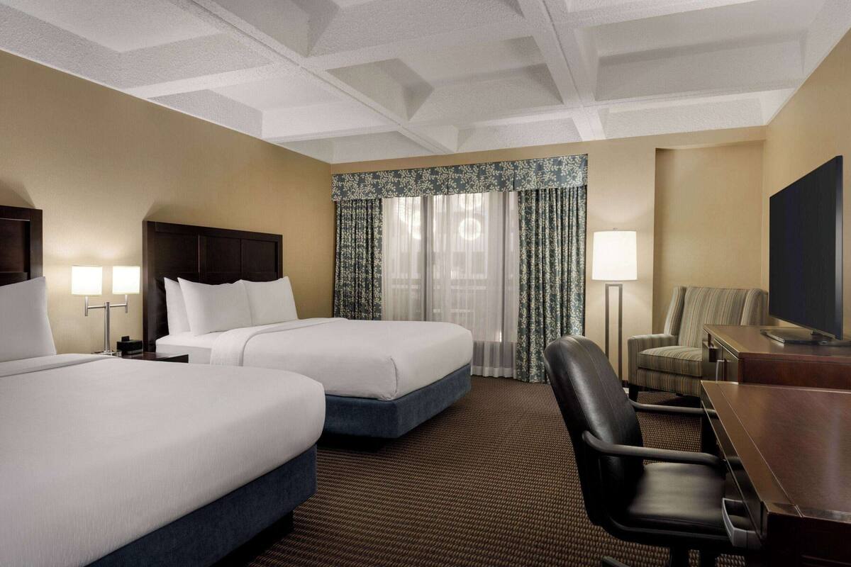 A hotel room with two beds, a desk, a chair, a television, and a window with curtains.