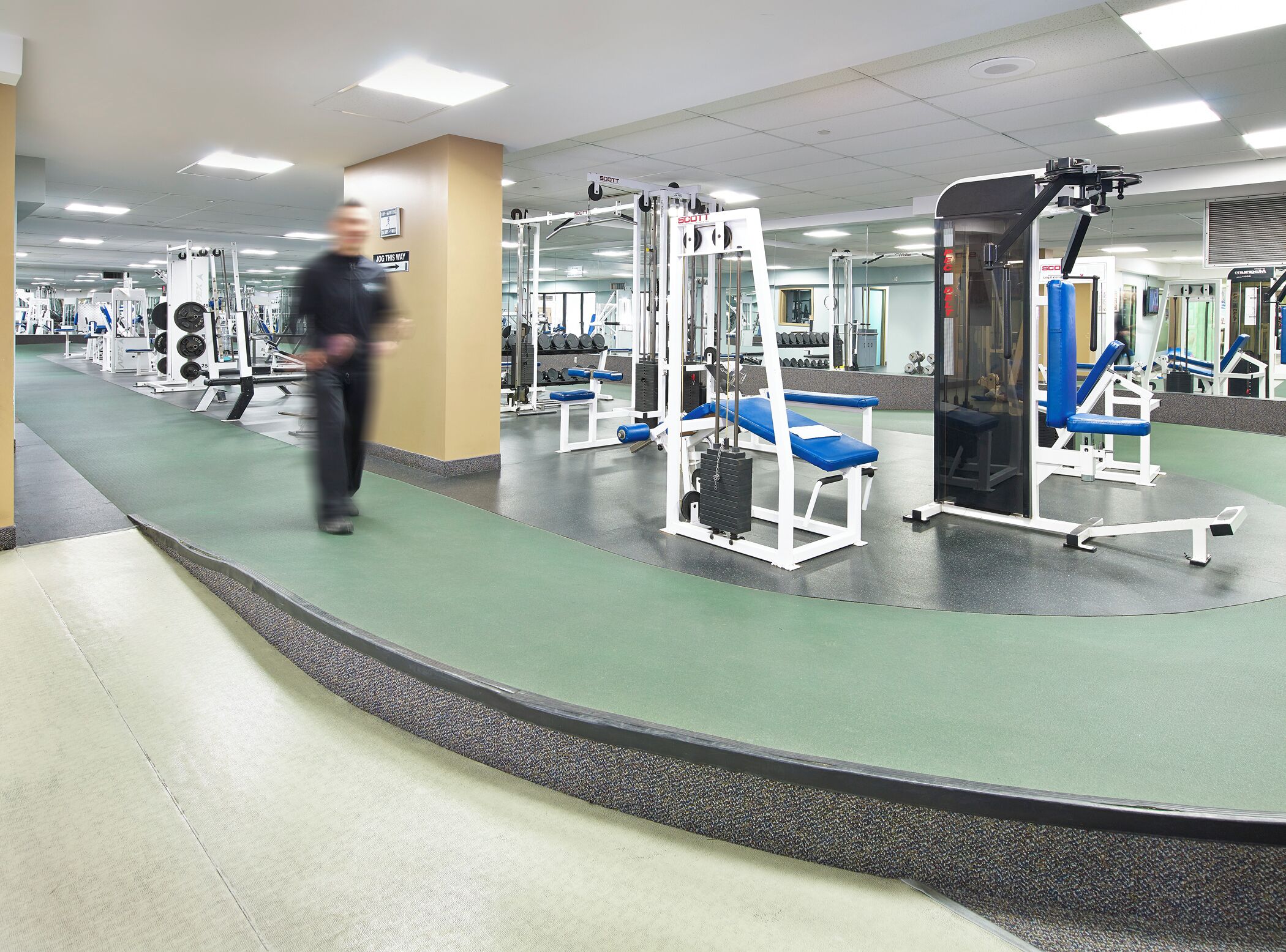 A gym with various exercise machines, a mirror wall, and a green floor.