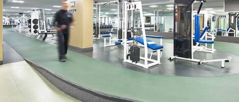 A gym with various exercise machines, a mirror wall, and a green floor.