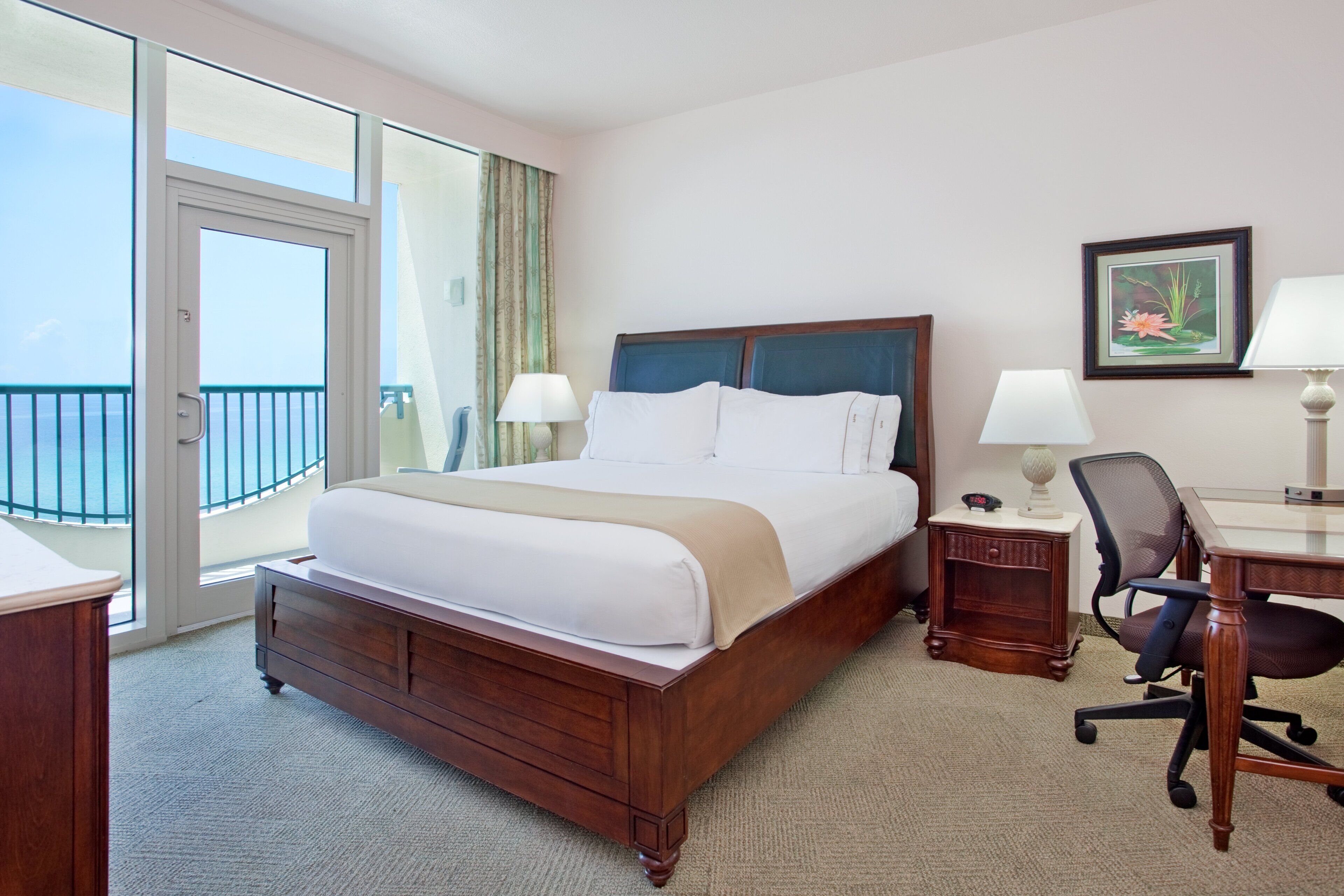 A hotel room with a large bed, a desk, a chair, a lamp, and a picture on the wall.